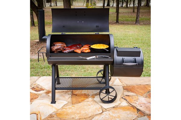 Коптильня Longhorn Offset Smoker с открытой крышкой на улице, внутри готовятся рёбра, курица и кукуруза в сковороде.